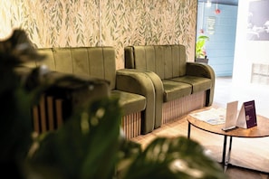 Un espace d’accueil avec un canapé vert, une table basse en bois et un mur orné d’un motif en bambou.