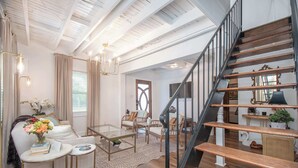 A spacious living area with a wooden staircase, a glass coffee table, and a comfortable seating arrangement. - Walk to Downtown Beaufort | 4BR Coastal Cottage (Beaufort)