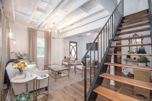 A spacious living area with a wooden staircase, a glass coffee table, and a comfortable seating arrangement. - Charming Coastal Cottage | Walk to Waterfront (Beaufort)
