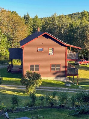A two-story wooden house with a red roof, a balcony, and a covered porch.