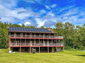 A two-story building with a balcony, solar panels, and a grassy yard.