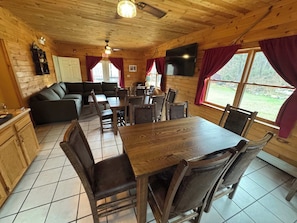 A wooden cabin interior with a dining table, chairs, a sofa, and a kitchen area.