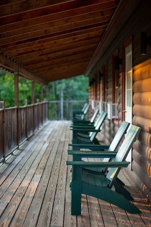 A covered porch with wooden flooring and green chairs.. Queen Room in Riverfront Lodge in West Forks