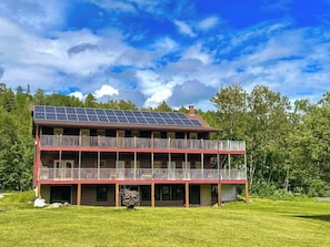 A two-story building with a balcony, solar panels, and a grassy yard.