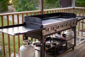 Ein tragbarer Grill auf einer Holzterrasse, zusammen mit einer Gasflasche und Kochgeschirr.