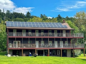 Un edificio de dos pisos con un balcón en cada planta, paneles solares en el techo y un área verde al frente.