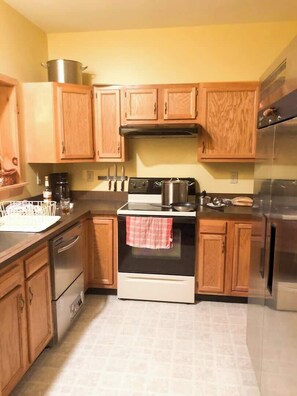 A kitchen with wooden cabinets, a stove, a refrigerator, and a coffee maker.