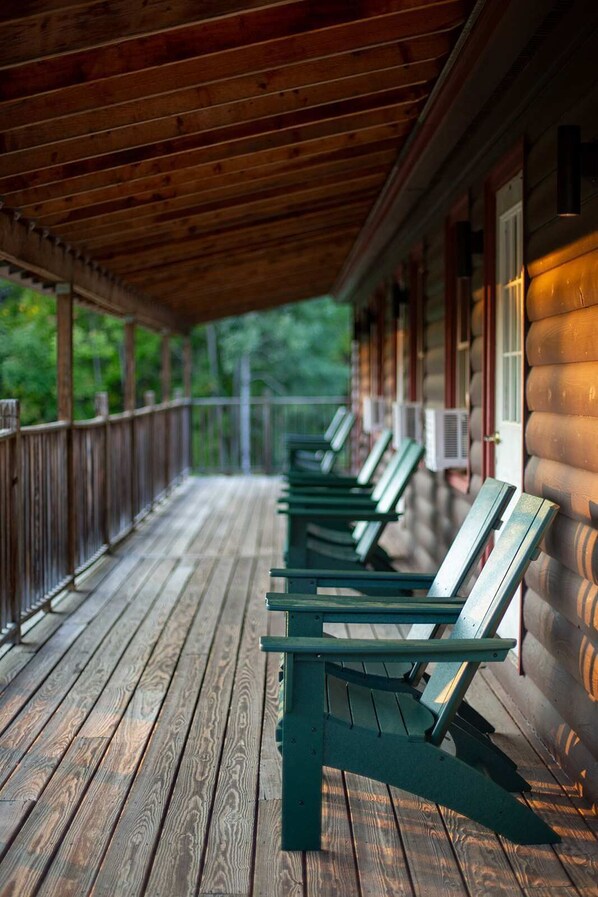 A covered porch with wooden flooring and green chairs.