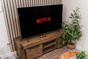 Ein Flachbildfernseher auf einem hölzernen TV-Schrank mit Fernbedienung, einer Blumentopf-Pflanze und einem gewobenen Korb.
