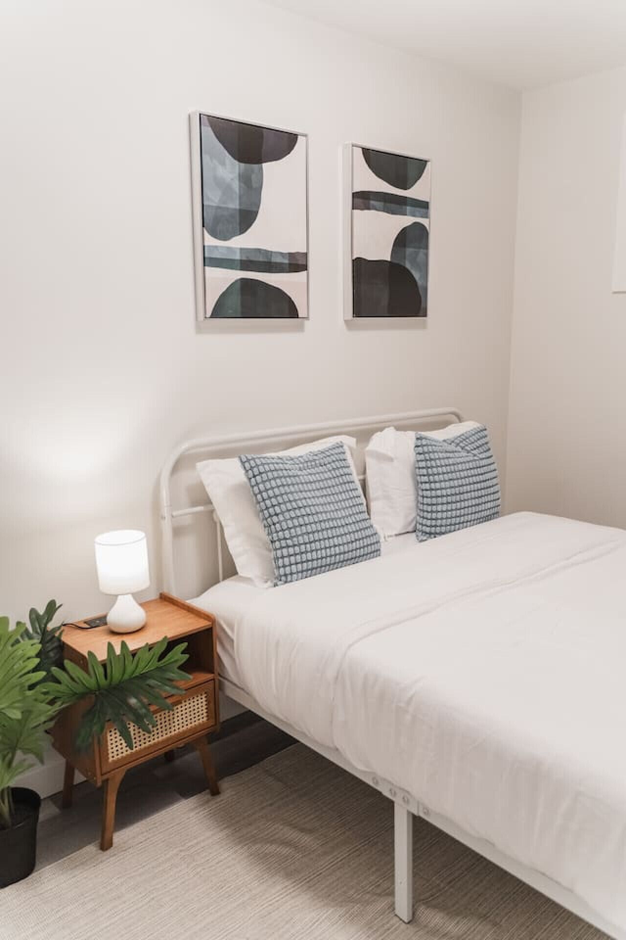 A bedroom with a bed, bedside table, lamp, and two abstract paintings on the wall.