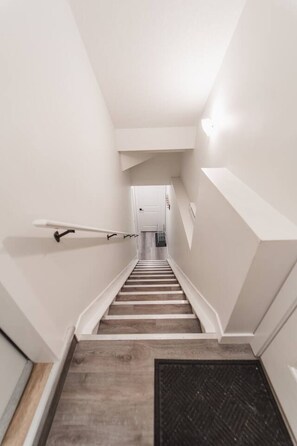 Eine enge Treppe mit Geländer auf der linken Seite, Holzboden und einem Lüftungsgitter unten.