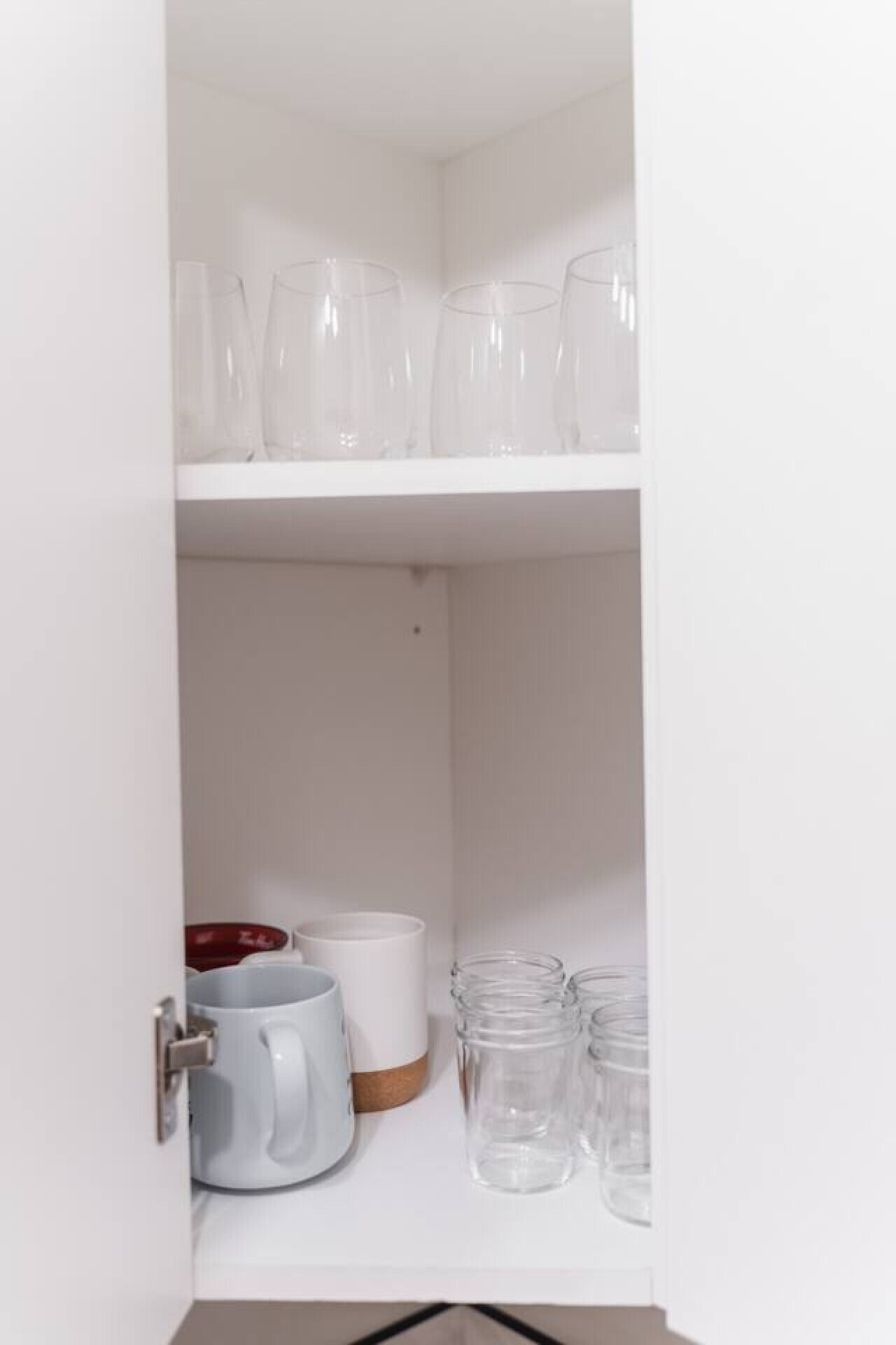 Ein weißes Schranksystem mit Regalen, auf denen klares Glasbesteck und eine weiße Tasse stehen.