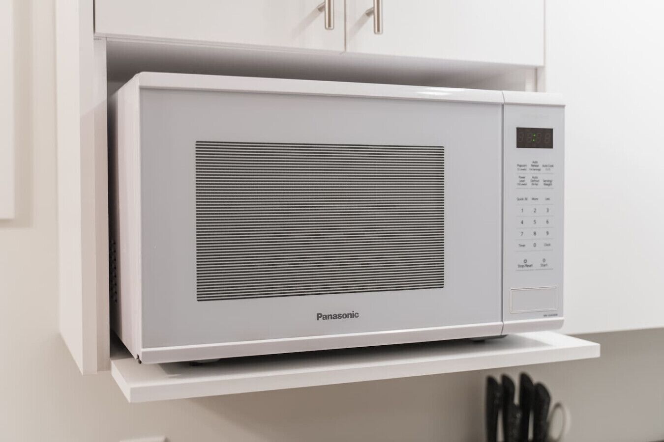 Un four à micro-ondes Panasonic blanc, doté d’un écran numérique et d’un panneau de commande, fixé sur un meuble blanc.