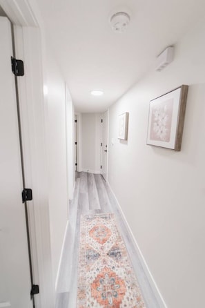 A hallway with white walls, a patterned rug, and framed artwork.