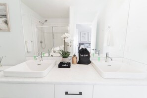 A bathroom with two sinks, a mirror, a shower, and a potted orchid. - Stylish Escape|9 Min to WEM|AC|Gym|Sauna & Patio (Edmonton)