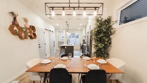 Un coin repas avec une table en bois dressée pour quatre personnes, des chaises noires, un luminaire suspendu et une plante en pot.