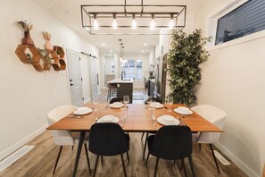 Un coin repas avec une table en bois dressée pour quatre personnes, des chaises noires, un luminaire suspendu et une plante en pot.
