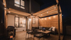 Une terrasse extérieure avec une plateforme en bois, un barbecue, une table avec des chaises et un canapé avec des coussins.