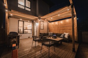 Une terrasse extérieure avec une plateforme en bois, un barbecue, une table avec des chaises et un canapé avec des coussins.
