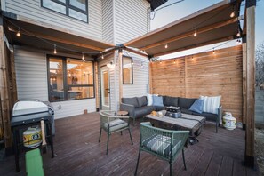 Eine überdachte Terrasse mit Holzboden, Gartenmöbeln und Lichterketten.