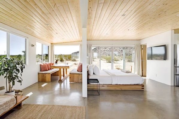 Un interno moderno con soffitto in legno, ampie finestre, un letto, zona pranzo e cucina.