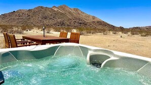 Un jacuzzi con mesa y sillas de madera, frente a un paisaje desértico con montañas al fondo.