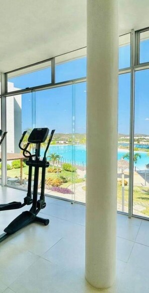 Et fitnessrum med en motionscykel og et stort vindue med udsigt over en pool og grøn bevoksning.