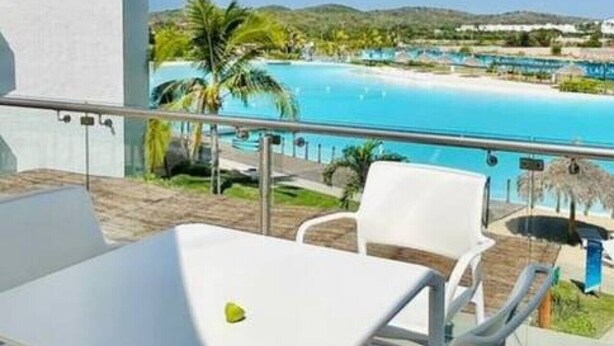 A balcony with a white table and chairs, overlooking a pool and greenery.