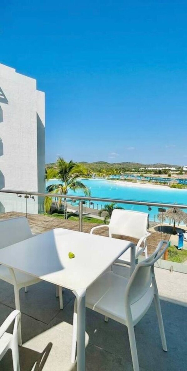A balcony with a white table and chairs, overlooking a pool and greenery.