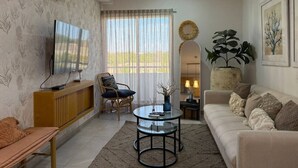 A living room with a sofa, a television, a round coffee table, a chair, and a large window with curtains.