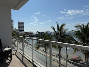 A balcony with a view of a beach, palm trees, and a clear sky.