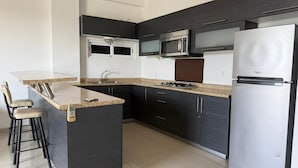 Eine moderne Küche mit dunklen Schränken, Edelstahlgeräten und einer Kücheninsel mit Granitplatte und Barhocker.