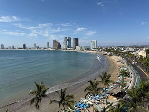 A coastal cityscape with a beach, palm trees, and modern buildings.