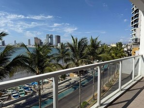 Ein Balkon mit Blick auf einen Strand, Palmen und eine Skyline mit hohen Gebäuden.