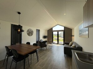 Een ruime kamer met een eethoek, een bank, een televisie en een groot raam.