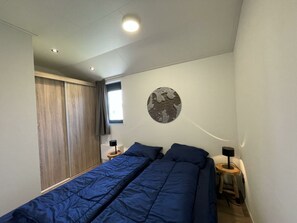 A bedroom with two beds, a window, a round wall decoration, and a ceiling light.