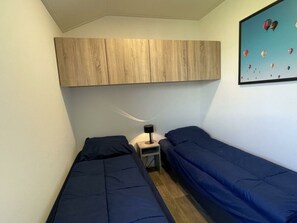 Een kleine, compacte kamer met twee eenpersoonsbedden, een nachtkastje, een wandkastje en een lijst met een afbeelding van luchtballonnen.