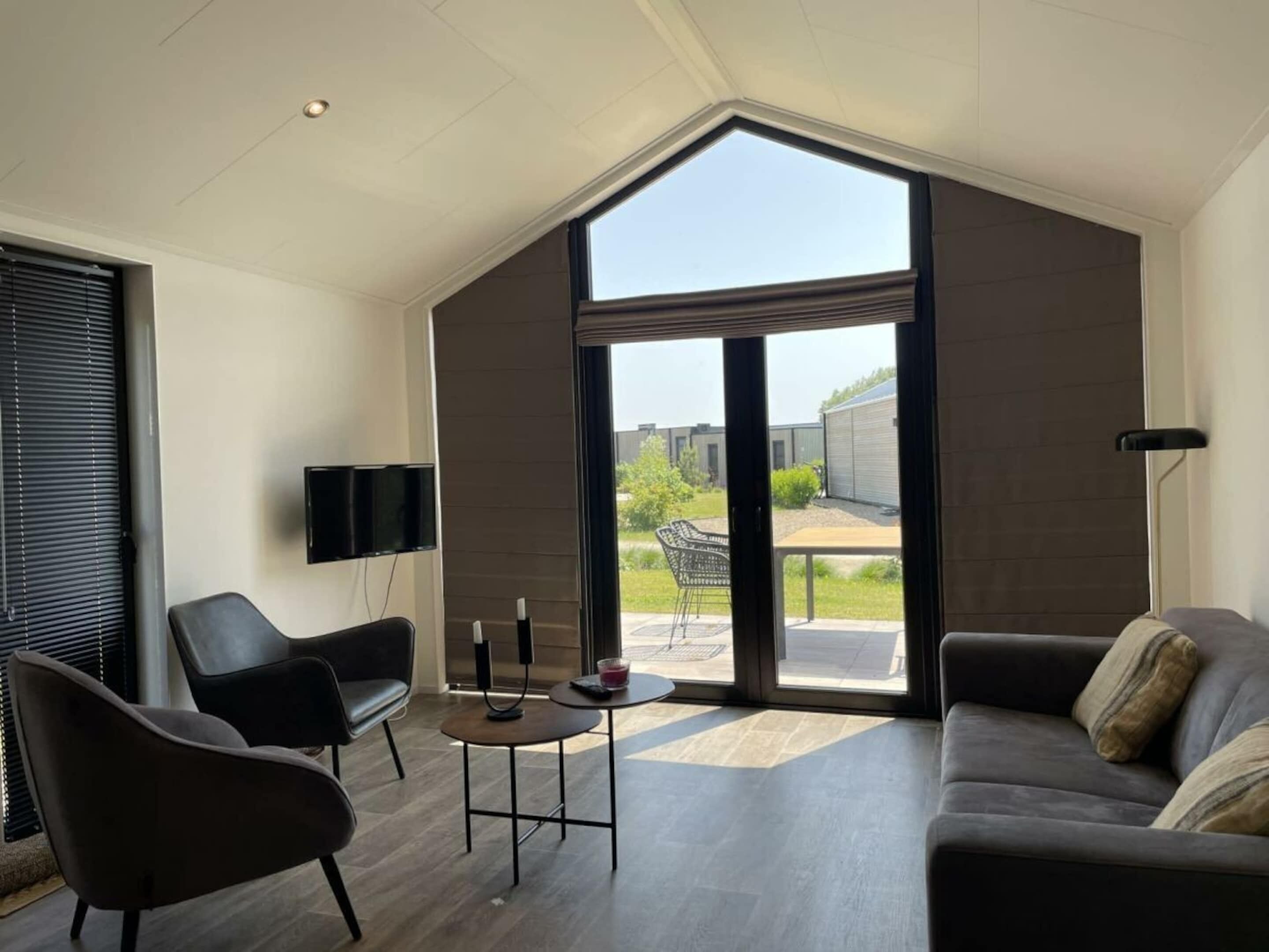 A modern living room with a large window, a flat-screen TV, a sofa, a chair, and a small table.