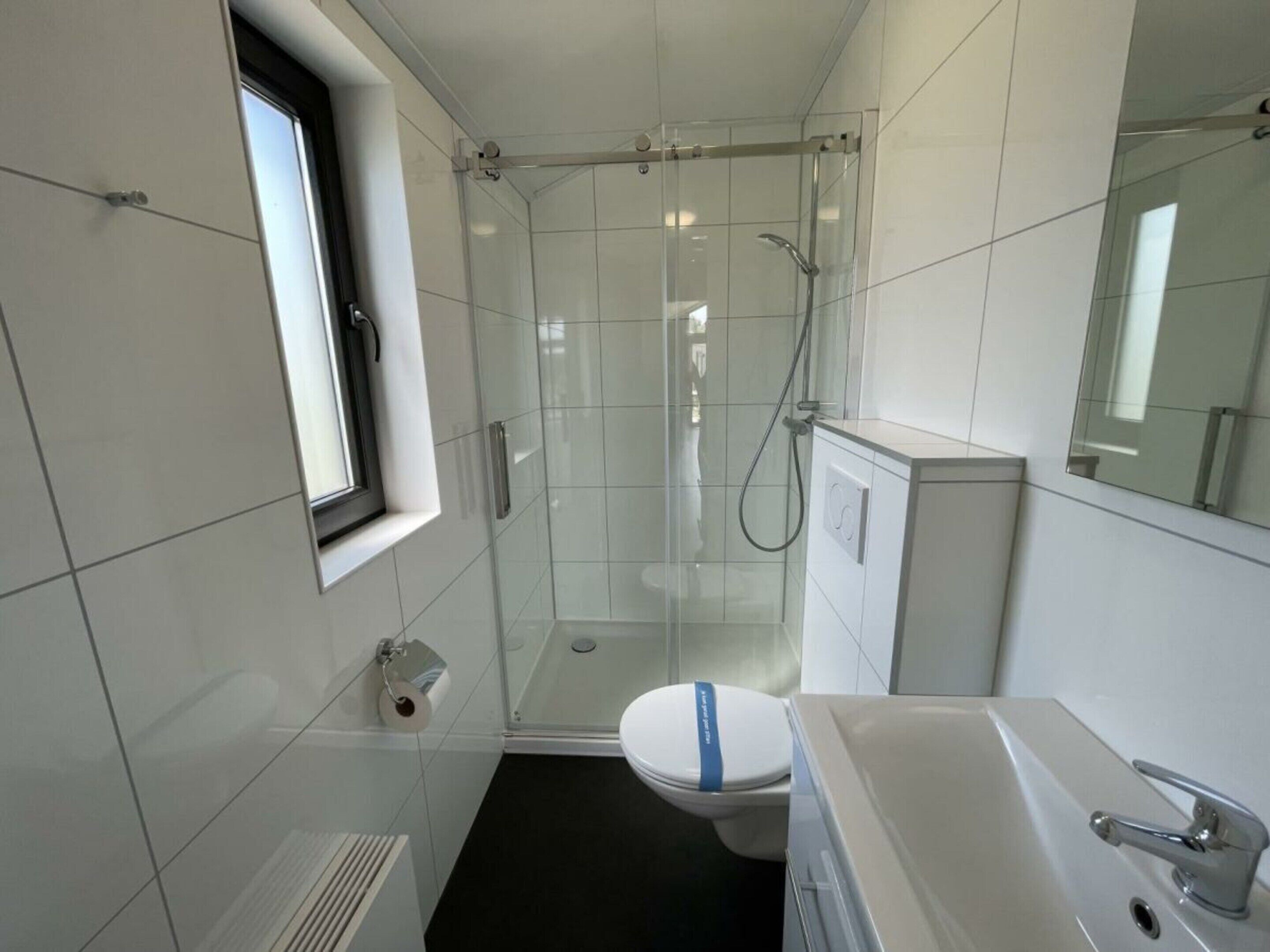 Un baño moderno con cabina de ducha de vidrio, inodoro, lavamanos y ventana.
