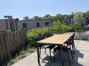 Een terras buiten met een houten tafel en stoelen, omgeven door een houten omheining en groen.