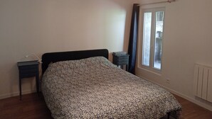 Una camera da letto con un letto, comodini, una lampada a sospensione, una finestra con tende e un termosifone.