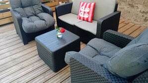 Un patio con mobili in vimini, un tavolino con un vaso di fiori e un pontile in legno.
