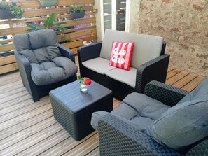 A patio with wicker furniture, a small table with a vase of flowers, and a wooden deck. - Renovated 130 m² house in Saint-Quirin with a terrace, pergola, and Wi-Fi; sleeps up to 8 people (Saint-Quirin)
