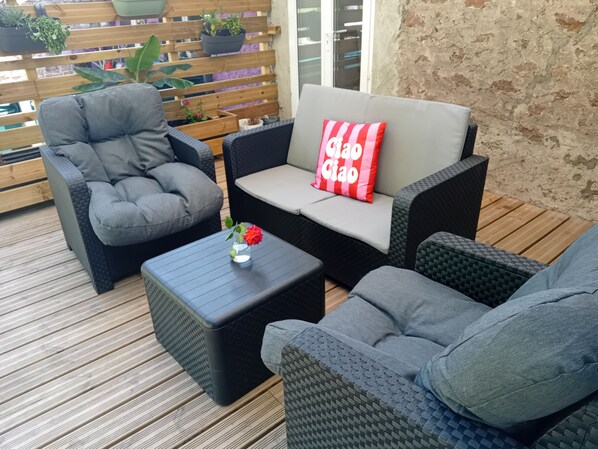 A patio with wicker furniture, a small table with a vase of flowers, and a wooden deck. - Renovated 130 m² house in Saint-Quirin with a terrace, pergola, and Wi-Fi; sleeps up to 8 people (Saint-Quirin)