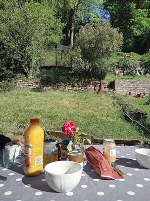 Une table recouverte d’une nappe à pois, une bouteille de jus d’orange, un vase avec une rose rouge, ainsi que divers pots et récipients.