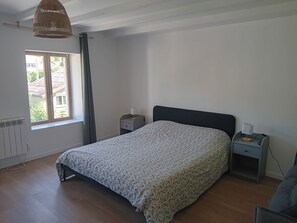A bedroom with a bed, two bedside tables, a window with curtains, a hanging light fixture, and a radiator. - Renovated 130 m² house in Saint-Quirin with a terrace, pergola, and Wi-Fi; sleeps up to 8 people (Saint-Quirin)