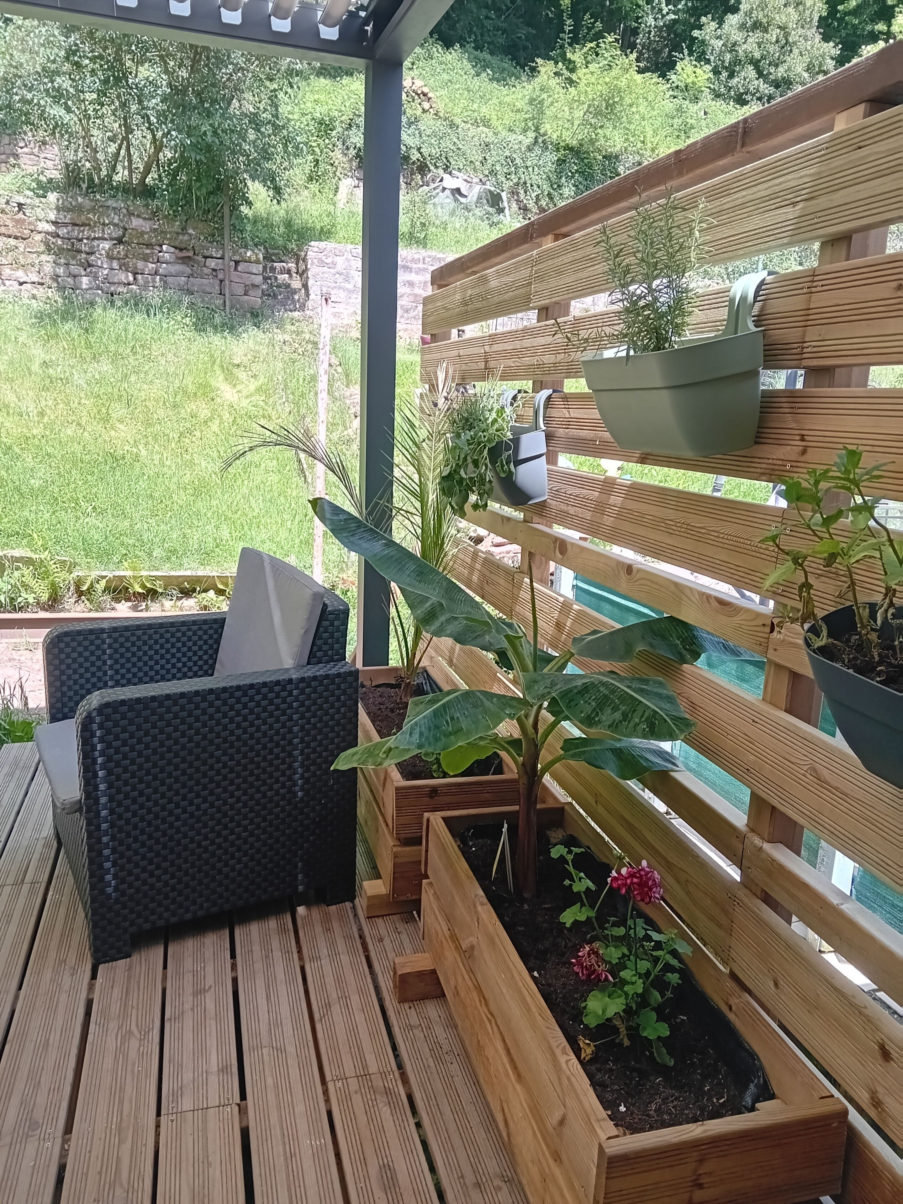 A wooden deck with outdoor furniture, raised garden beds with plants, and a wooden fence.