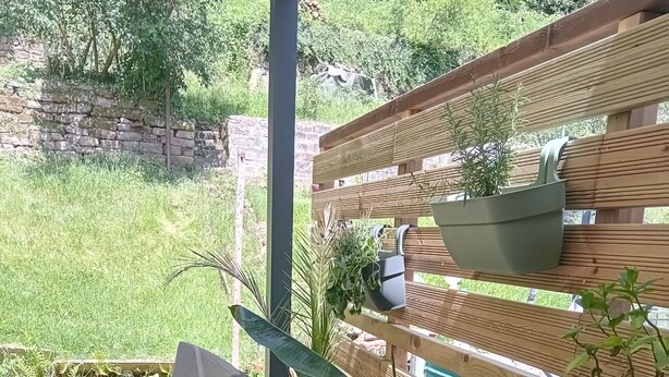 Un terrazzo in legno con mobili da esterno, aiuole rialzate con piante e una recinzione in legno.
