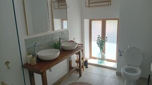 Un bagno con due lavandini, un water, uno specchio e una finestra.