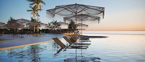 Zona de piscina con sillas de descanso, sombrillas y vista al mar.